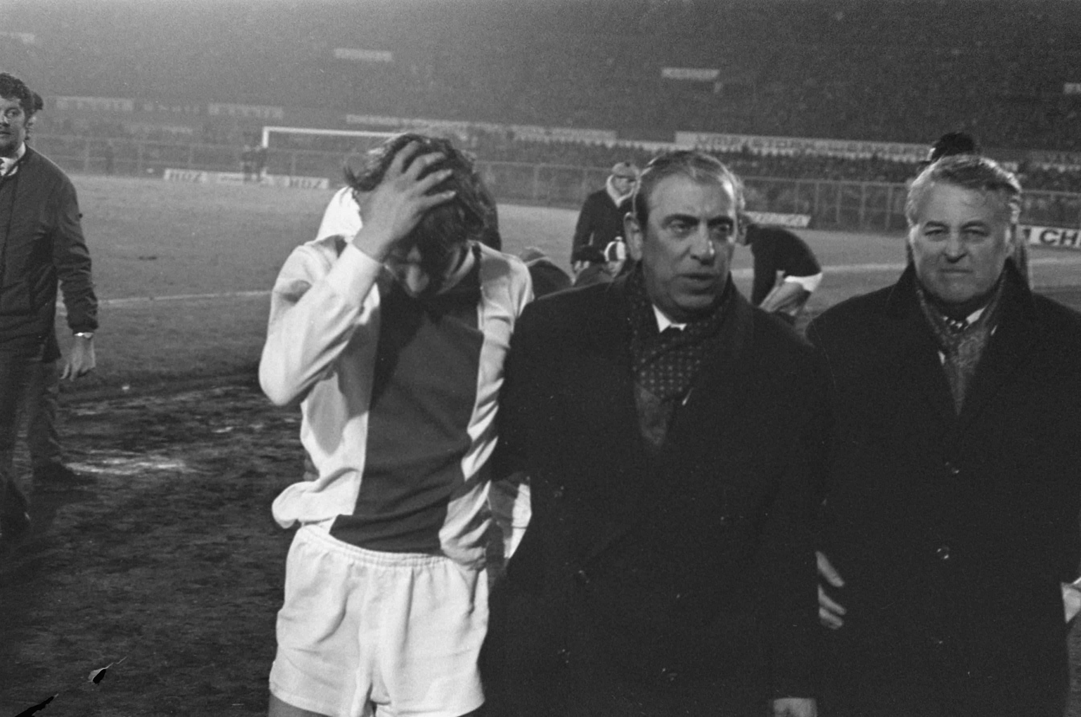 Eine Gruppe von Männern steht zusammen auf einem Fußballfeld, im Hintergrund ist ein Stadion zu sehen, auf einem Schwarz-Weiß-Bild.