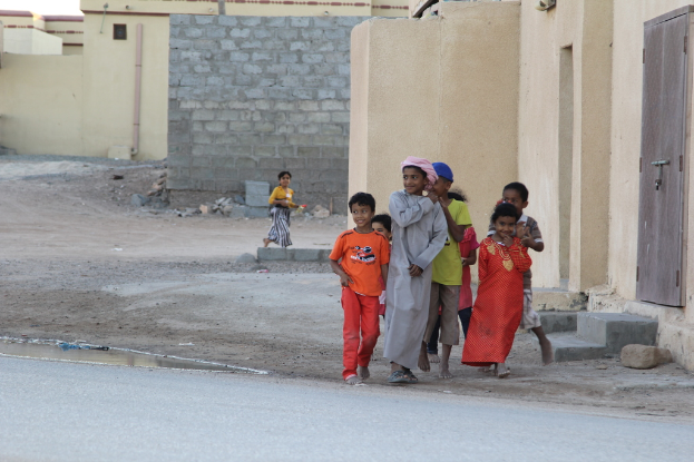 Eine Gruppe strahlender Kinder, die sich im Freien mit Gebäuden, Wasser, Felsen und einer Straße im Hintergrund befinden.