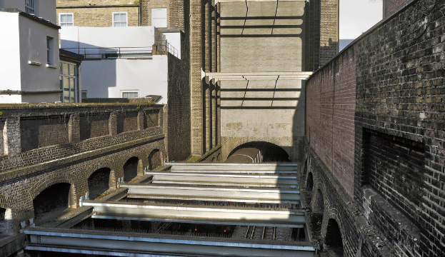 Ein Zug fährt durch einen Tunnel mit Gebäuden im Hintergrund.