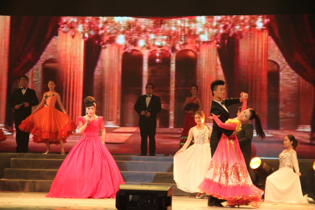 Eine Gruppe von Menschen auf einer Bühne mit Scheinwerfern, Stufen und einem Hintergrundbild, mit einem Lautsprecher unten, was auf eine Tanzvorstellung hindeutet.