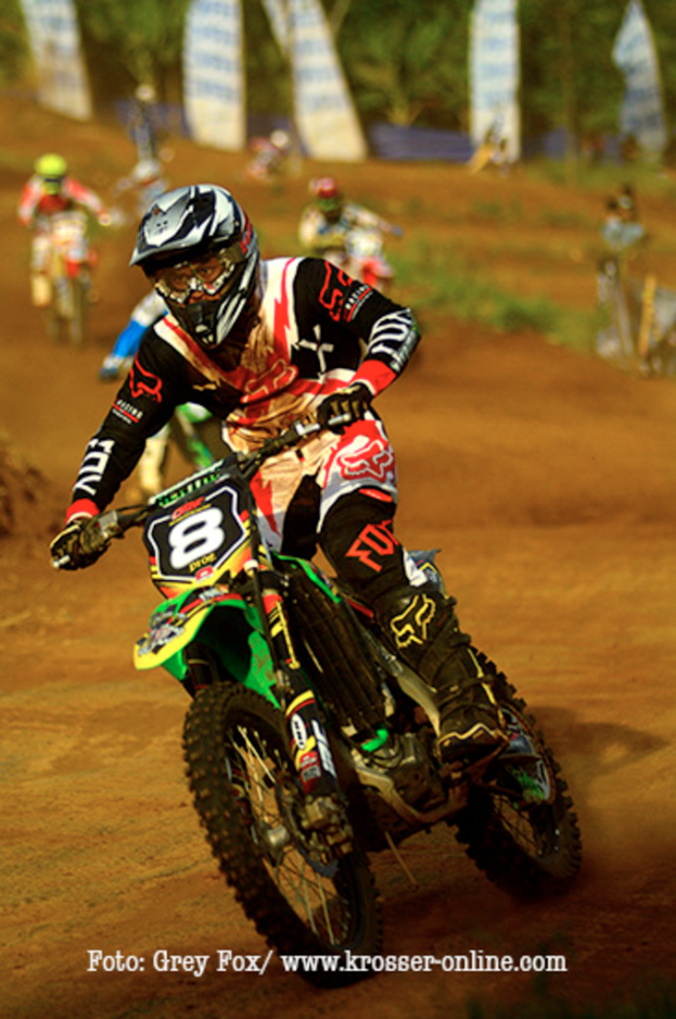 Mehrere Motorradfahrer mit Helmen rennen auf einer Rennstrecke, mit Text am unteren Bildrand.