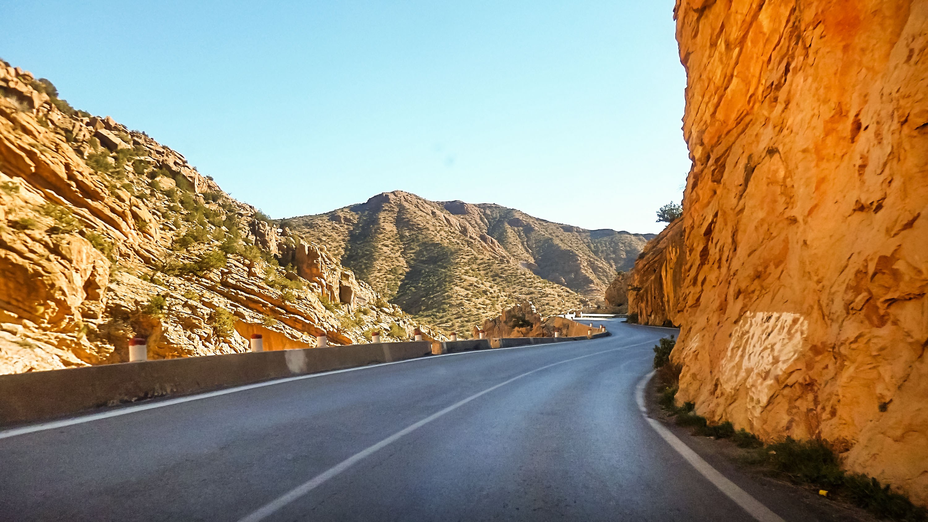 Winding road through a rocky gorge with hills on either side under a clear blue sky.