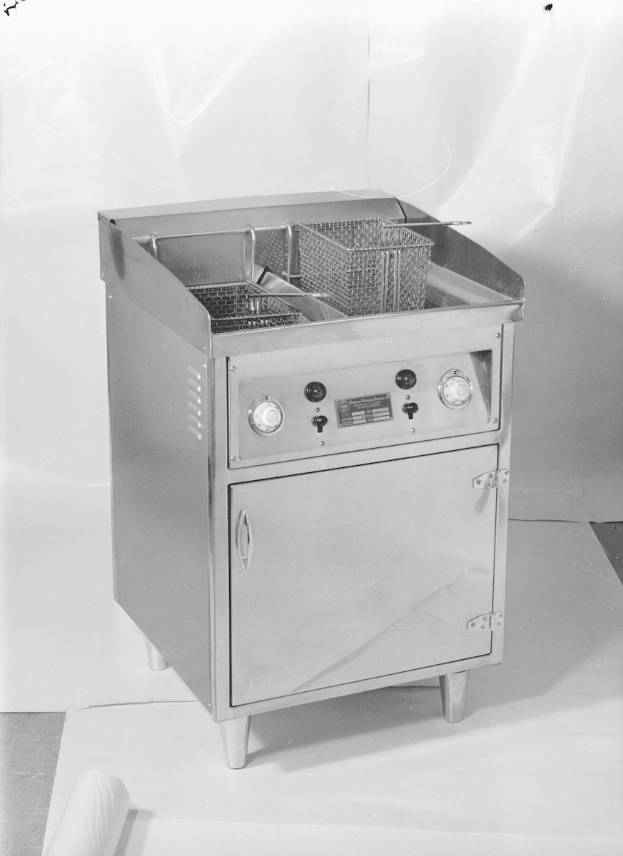 Ein Schwarz-Weiß-Foto eines Gasfritiers mit einem Korb oben drauf, das auf einem Tisch steht.