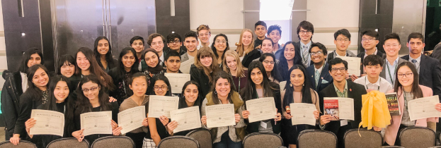 Eine Gruppe von Menschen posiert mit Urkunden vor Stühlen und einer Wand, wahrscheinlich bei einer Abschlussfeier 2019-2020.