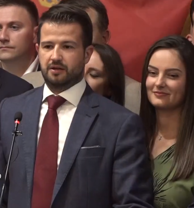 Ein Mann im Anzug und Krawatte steht an einem Rednerpult und hält eine Rede vor einer Menge mit einem Banner im Hintergrund, wahrscheinlich als Reaktion auf ein Regierungverbot von Social Media.