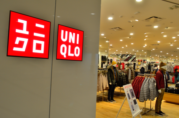 Das Innere eines Uniqlo-Geschäfts mit Puppen in Jacken, Kleidung an Bügeln, Informationsschildern, Deckenleuchten und einer Person mit Schuhen.