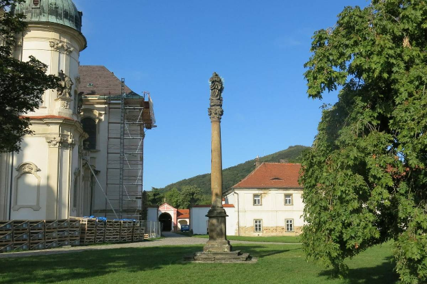 Eine Säule steht in einem grünen Feld in Heidelberg, Deutschland, mit einem Gebäude, Bäumen, einem Hügel und dem Himmel im Hintergrund.