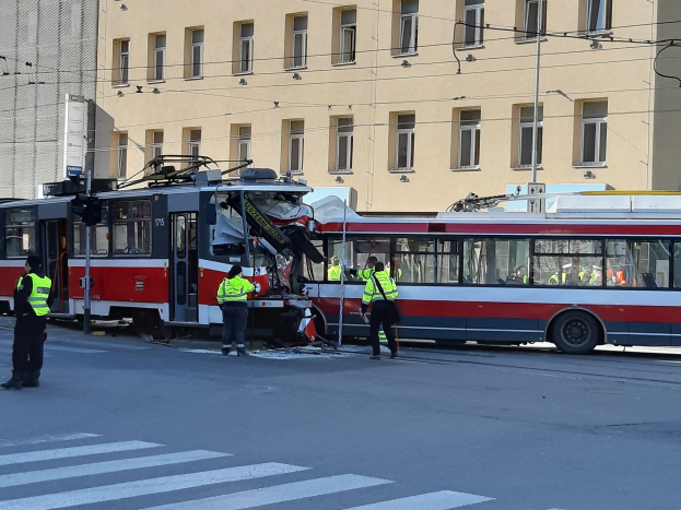 Eine rote und weiße Straßenbahn ist auf der Seite der Straße verunglückt, mit ein paar Menschen in der Nähe und einem Gebäude im Hintergrund.