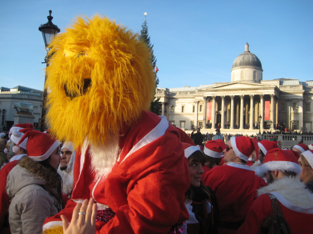 Person in Santa-Kostüm mit Tiger-Maske steht mit anderen in Santa-Kostümen vor einem Gebäude.