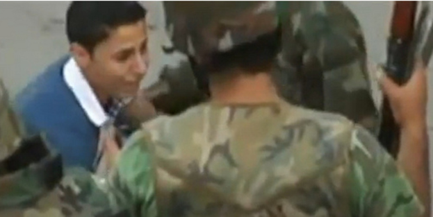 Ein Militärangehöriger in der Mitte hält eine Waffe, mit einem Jungen vor ihm und einem weiteren Militärangehörigen links daneben.