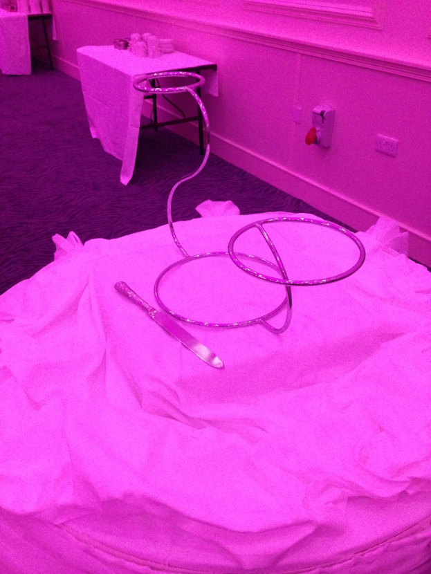 Ein Messer und verschiedene Gegenstände sind auf einem Tuch in der Mitte des Bildes angeordnet, mit einem Tisch mit weiteren Gegenständen und einer Wand im Hintergrund und einem Teppich unten.