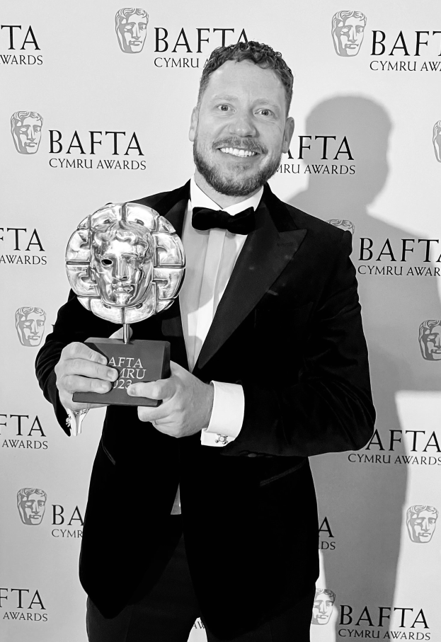 Ein Mann im Smoking, der eine BAFTA-Trophäe hält und vor einer Tafel mit der Aufschrift "BAFTA Awards 2018" steht.