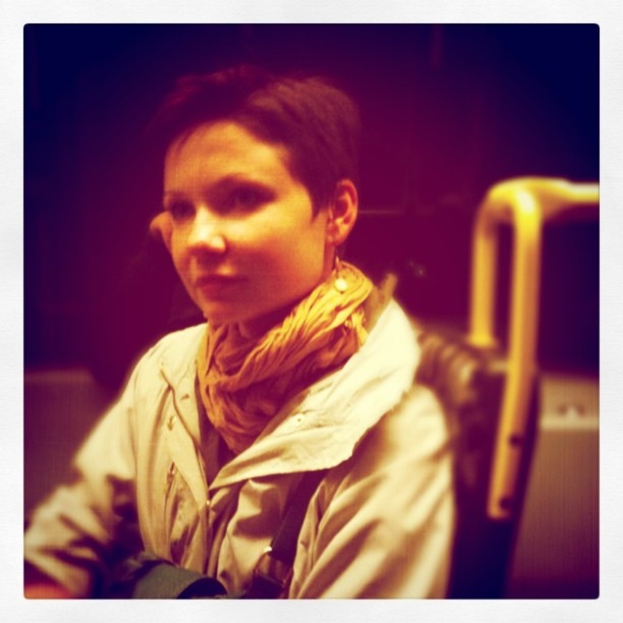 Eine Person sitzt, trägt einen Mantel und einen Schal.