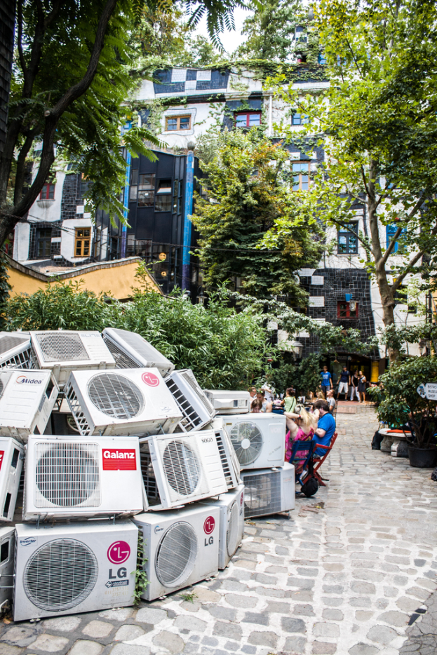 Luftkühler auf dem Boden links unten, eine Spur nach rechts, Menschen auf Stühlen neben der Spur, mit Gebäuden, Bäumen und Pflanzen oben.