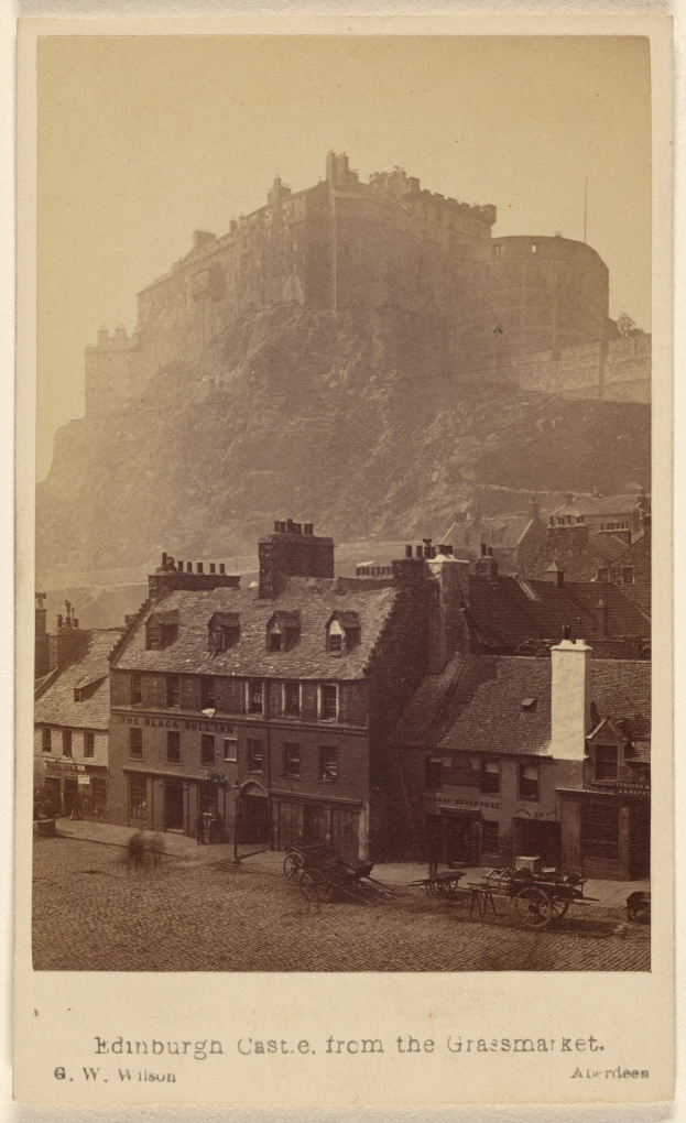 Altes Foto von Edinburgh Castle aus der Sicht vom Grassmarket, mit Gebäuden und Karren im Vordergrund und einem Hügel im Hintergrund; Text ist am unteren Bildrand sichtbar.