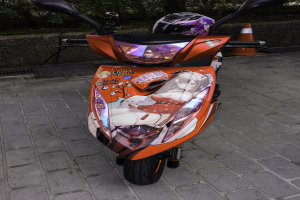 Oranges E-Scooter auf der Straße geparkt mit einem Helm darauf, neben einem Verkehrskegel, einer Wand und Bäumen im Hintergrund.