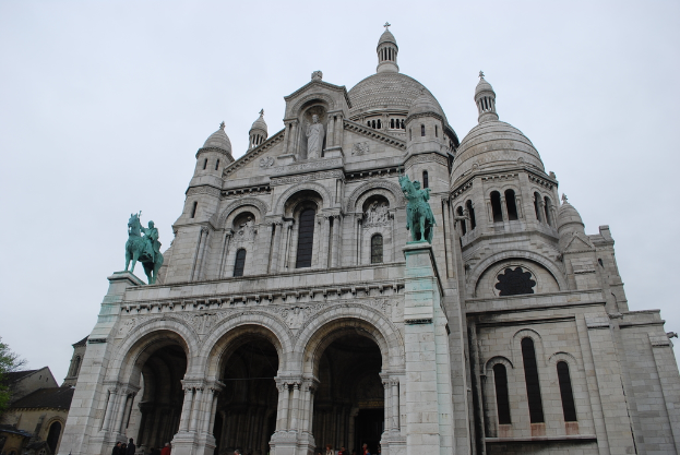 Ein Denkmal steht in der Bildmitte, mit Häusern und einem Baum in der linken unteren Ecke.