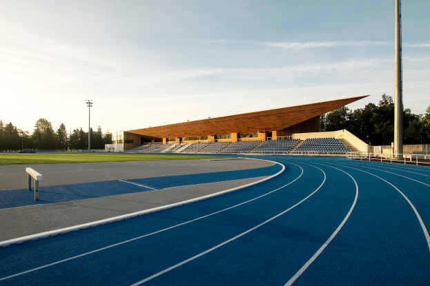 Eine blaue Laufbahn an der University of California, Berkeley, mit einer hölzernen Struktur in der Mitte, umgeben von Gras, Pfählen, Lichtern und Bäumen, unter einem bewölkten Himmel.