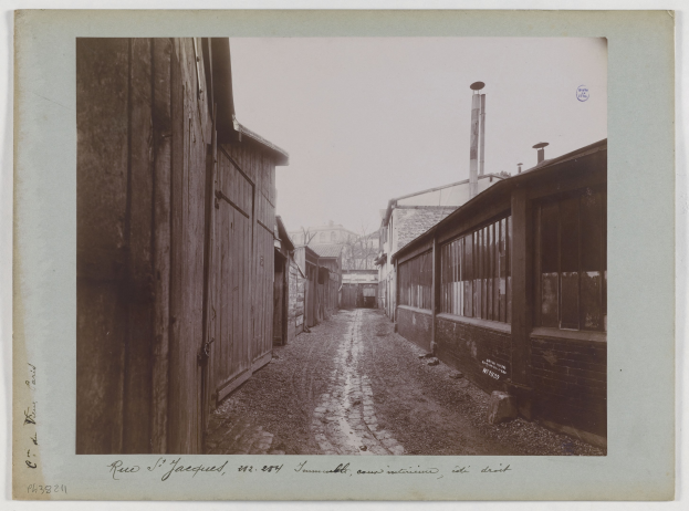 Ein altes Schwarz-Weiß-Foto einer Schotterstraße mit Gebäuden auf beiden Seiten und Text am unteren Rand des Bildes.