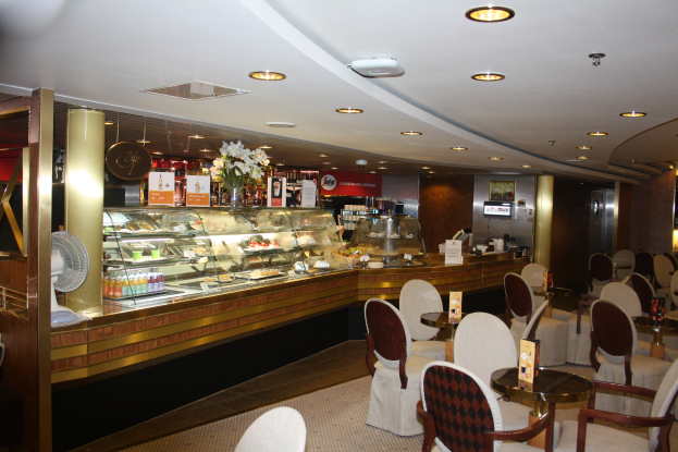 Ein Restaurant-Innenraum mit Tischen und Stühlen, einer Theke mit Blumenvasen, Texttafeln, einem Ventilator und anderen Gegenständen unter einer Decke mit warmem Licht.