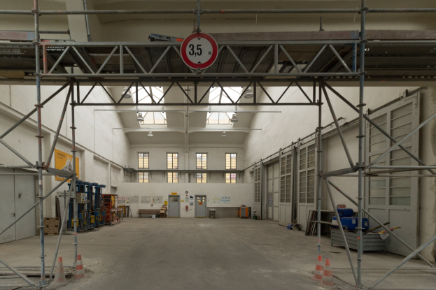 Großes Lagerinneres mit ausgedehnten Gerüsten, Verkehrszeichen, Metallstangen, einem Schild, Maschinen, einer Tür, Fenstern, Wänden, Deckenleuchten und einem Dach.