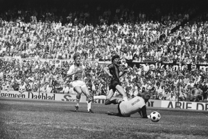 Schwarzes und weißes Foto von Fußballspielern im Einsatz auf einem Feld mit Zuschauern im Hintergrund und einem Bundesliga-Banner mit der Aufschrift "Bundesliga 1978-79 Ajax 1-1 Hannover 96."