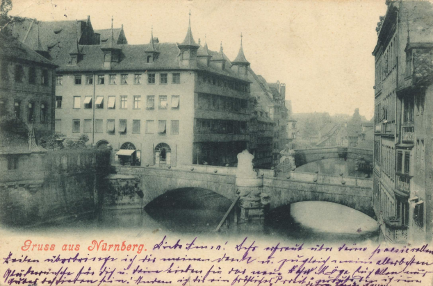 Ein altes Foto einer Brücke, die einen Fluss in Nürnberg, Deutschland, überspannt, mit umgebenen Gebäuden und einem sichtbaren Himmel, und Text am unteren Bildrand.