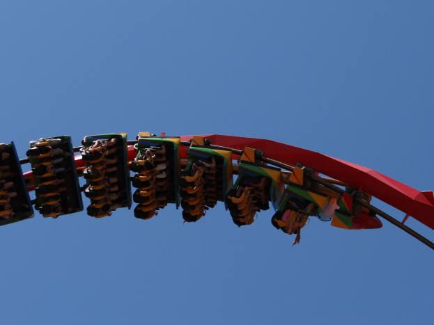 Menschen auf einer buntfarbenen Achterbahn gegen einen hellblauen Himmel.