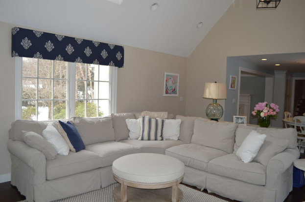 Ein Wohnzimmer mit einer Couch, Kissen, einem Tisch, Stühlen, einem Blumenstrau√ü, einem Foto Rahmen, einer Alarm Uhr und einem Fenster auf der linken Seite mit Deckenlichtern.