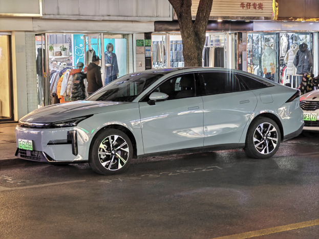 Elektrischer Mitsubishi Lancer EV auf einer nächtlichen Stadtstraße geparkt, umgeben von Gebäuden, beleuchteten Schaufenstern, Schaufensterpuppen in Kleidern und Schildern.