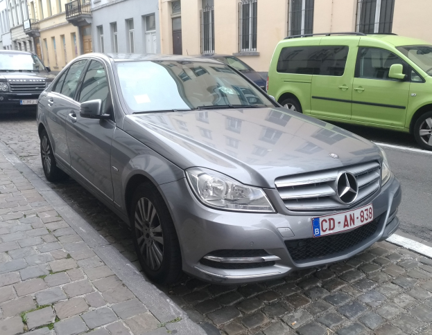 Ein Mercedes-Benz C 220 CDI BlueEfficiency Avantgarde, der auf einer von Gebäuden gesäumten Straße fährt, mit Fenstern, Geländern und Namensschildern, unter einem sichtbaren Himmel.