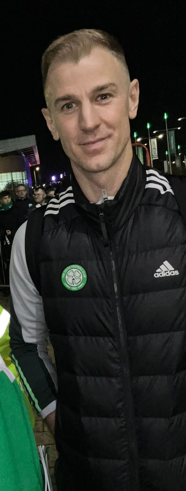 Ein Mann in einer schwarzen Jacke steht lachend vor einer Menge, beleuchtet von Gebäudelichtern und dem Himmel, wahrscheinlich feiernd nach dem Sieg von Celtic im schottischen Pokalfinale.