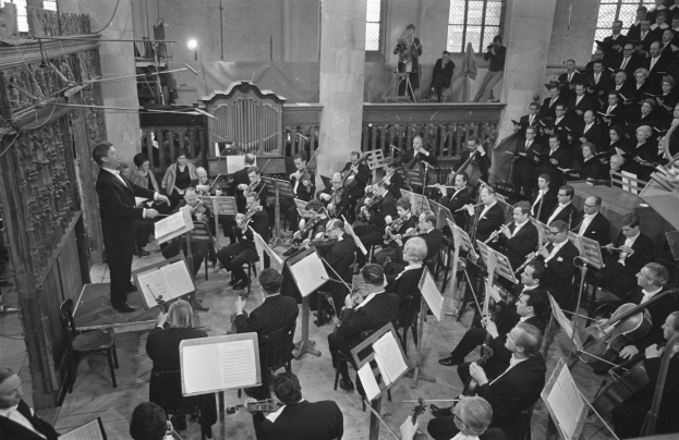 Schwarzes und weißes Bild einer Gruppe von Menschen, die in einer Kirche Musikinstrumente spielen, die auf Stühlen sitzen und stehen, mit Notenpulten vor ihnen.