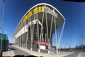 Das Europa-Park-Stadion in Barcelona, Spanien, ein großes Gebäude mit Text darauf, umgeben von Pfählen, Lampen, Bäumen und einem Zaun, mit dem Himmel im Hintergrund.