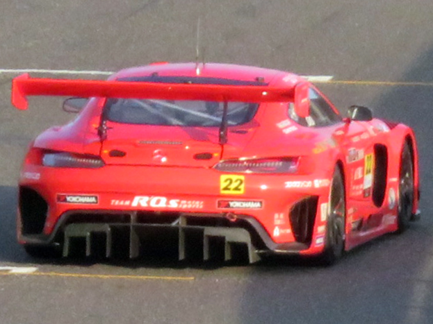 Roter Porsche 911 GTS Rennwagen auf einer Rennstrecke mit großem Heckflügel und Spoiler, niedriger Profil, breiter Stand und schwarzen Rädern.