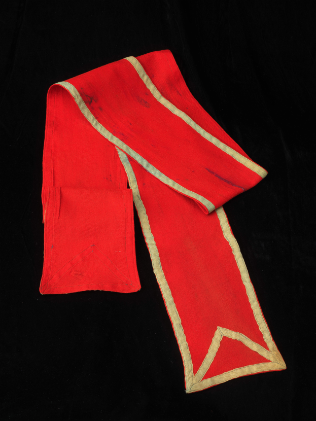 Eine rote Stola mit goldener Borte auf schwarzem Hintergrund.