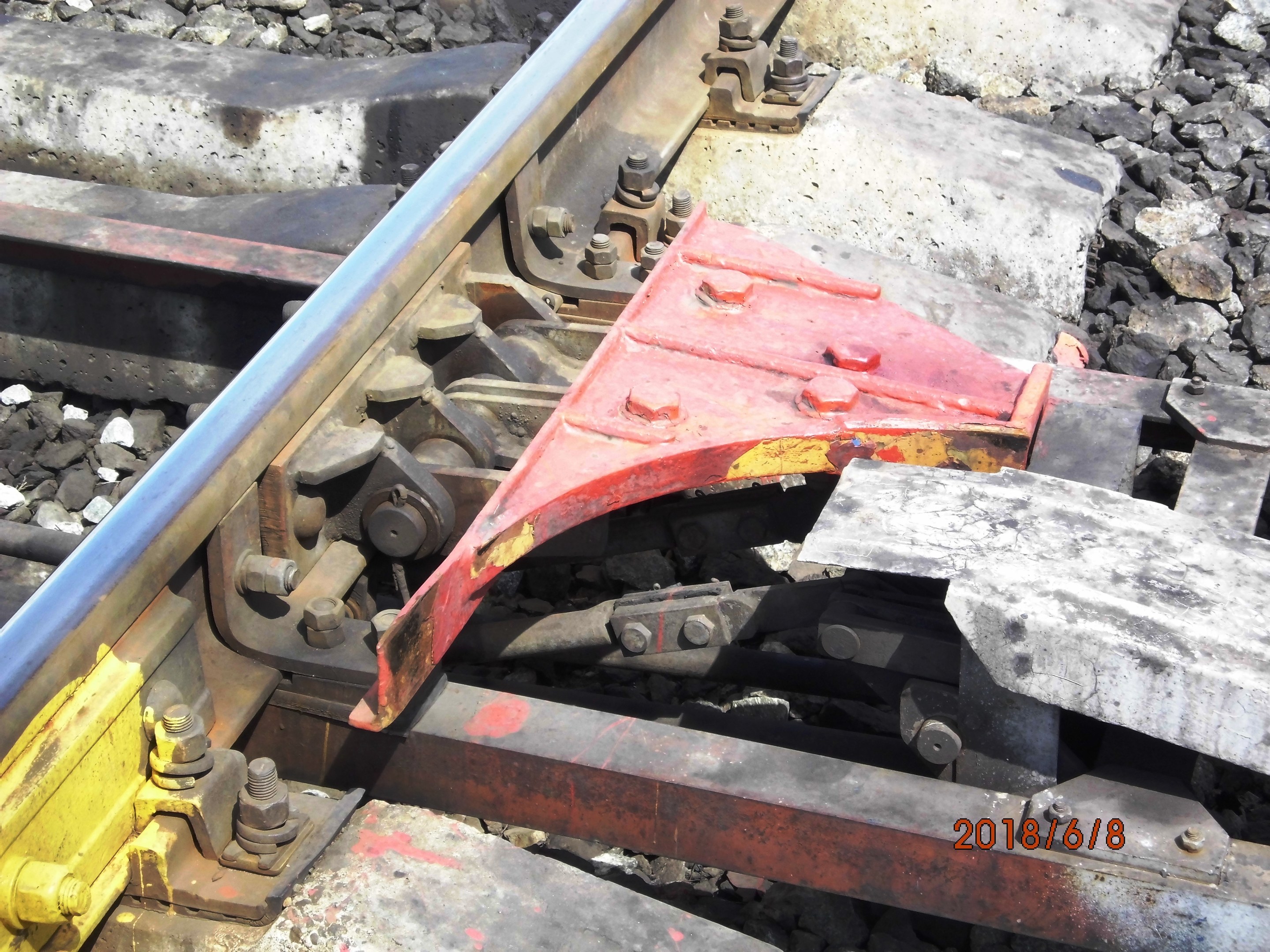 Nahaufnahme einer Schienenstrecke mit einem Metallschutzbauteil und Schottersteinen.