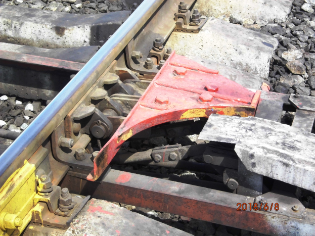 Nahaufnahme einer Schienenstrecke mit einem Metallschutzbauteil und Schottersteinen.