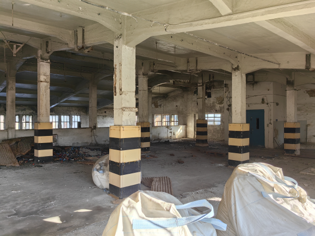 Ein verlassenes Gebäude in einem schlechten Zustand mit Schutt, darunter Taschen, die auf dem Boden verstreut sind, mit zerbrochenen Fenstern, einer Tür und einem Dach.