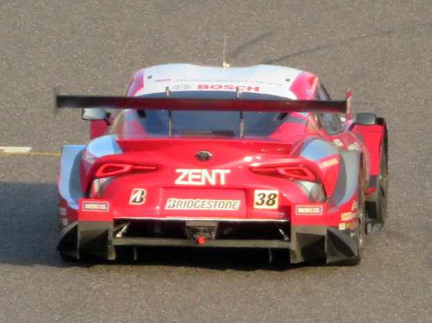 Ein rotes Sportauto mit Text und Zahlen, das beim 24-Stunden-Rennen von Le Mans teilnimmt, fährt auf einer Rennstrecke.