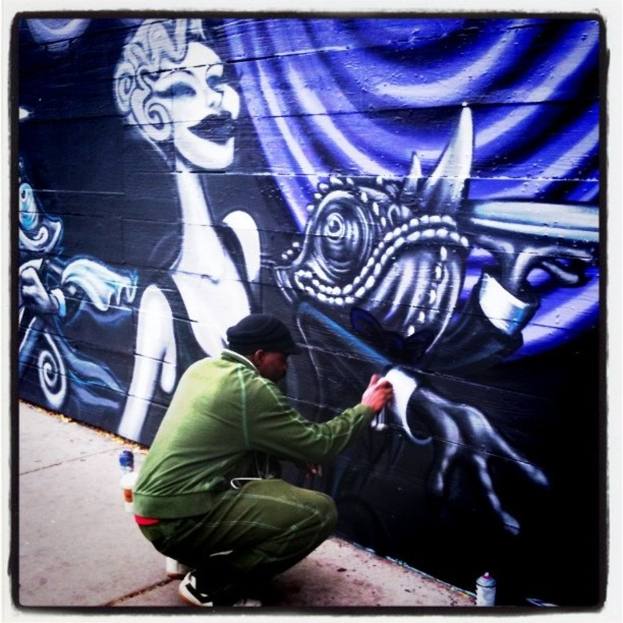 Eine Person mit einer Flasche in der Hand steht auf einer Straße, umgeben von mehreren anderen Flaschen, mit einer graffiti-bedeckten Wand im Hintergrund.