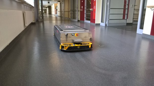 Ein Reinigungsroboter steht auf dem Boden eines Gebäudes, umgeben von Wänden, Türen, Lampen und anderen Gegenständen.