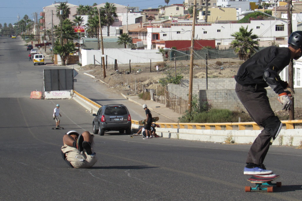 Eine Straße mit Menschen, die Schlittschuh laufen, geparkten Fahrzeugen und Häusern und Bäumen im Hintergrund.