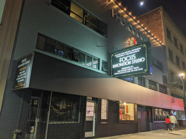 Außenansicht des Focus Innovation Studios in New York City bei Nacht, mit erleuchteten Fenstern, Straßenlaternen, Fußgängern auf dem Gehweg und umliegenden Gebäuden.