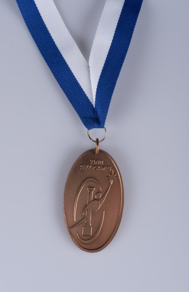 Goldmedaille mit blauen und weißen Bändern auf weißem Hintergrund mit eingravierter Schrift.