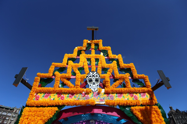 Ein Día de los Muertos-Bogen, geschmückt mit Blumen und einem Schädel, steht in Mexiko-Stadt, eingerahmt von Gebäuden und einem klaren blauen Himmel.