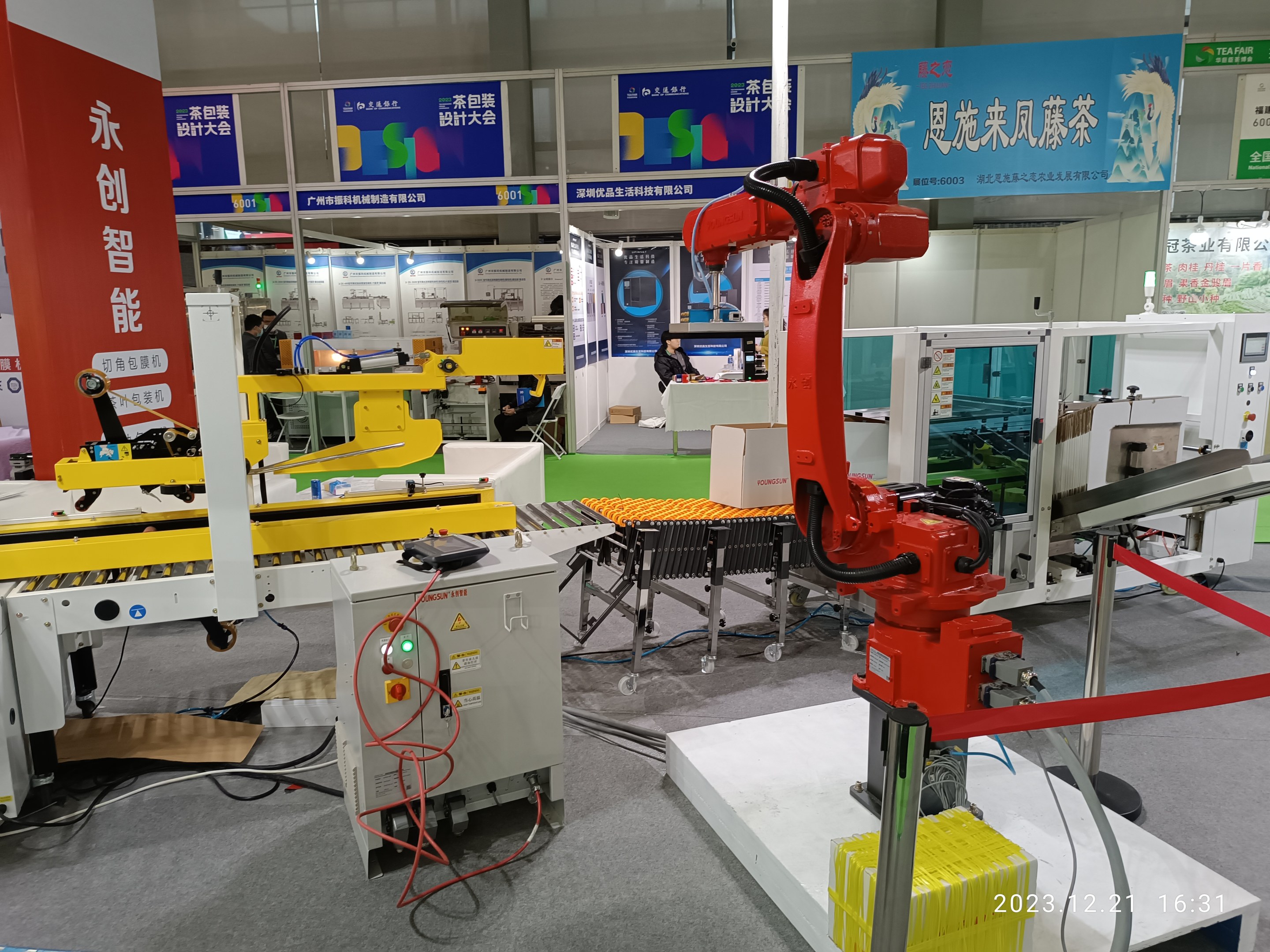 Eine Gruppe von Robotern auf einem Tisch in einer Fabrikumgebung umgeben von Maschinen, Kabeln, Texttafeln und Lampen, mit Menschen im Hintergrund.