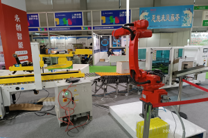 Eine Gruppe von Robotern auf einem Tisch in einer Fabrikumgebung umgeben von Maschinen, Kabeln, Texttafeln und Lampen, mit Menschen im Hintergrund.