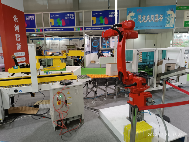 Eine Gruppe von Robotern auf einem Tisch in einer Fabrikumgebung umgeben von Maschinen, Kabeln, Texttafeln und Lampen, mit Menschen im Hintergrund.