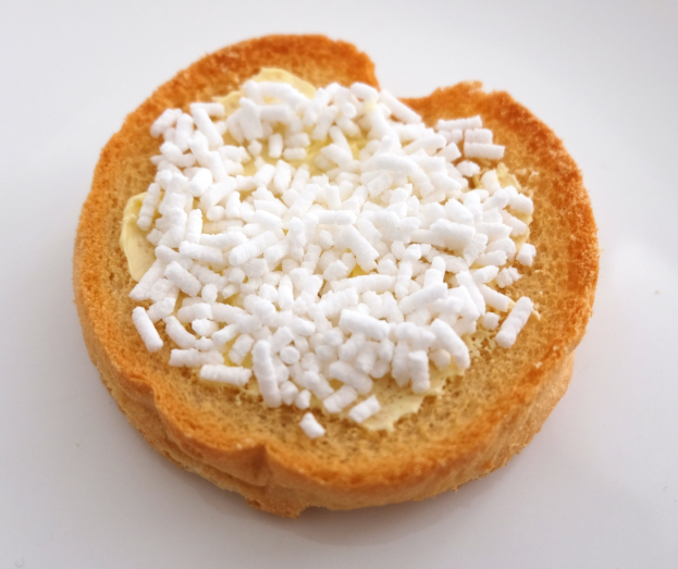 Herzförmiges Brotscheibchen mit Butter und Zucker auf einer weißen Oberfläche.